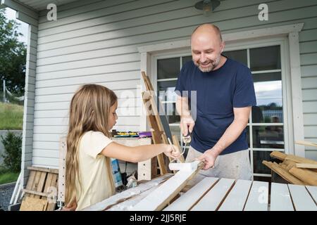 Smiling man painting planks with daughter in back yard Stock Photo