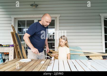 Daughter looking at father painting planks in back yard Stock Photo