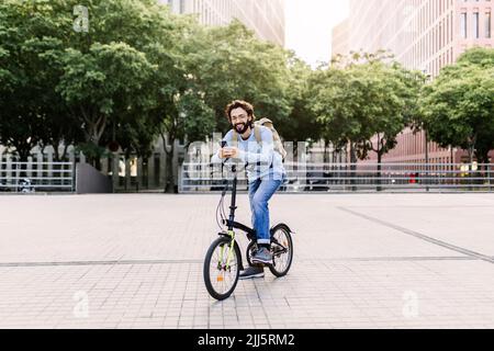 Smiling man using phone sitting on bicycle Stock Photo