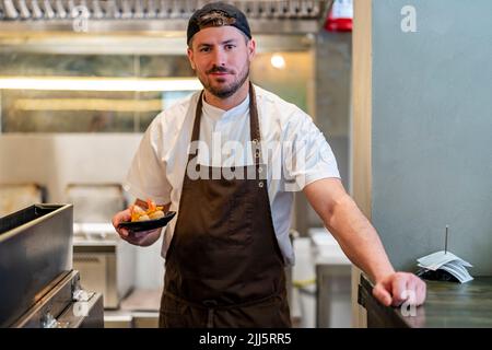Smiling chef with food in plate standing at kitchen of restaurant Stock Photo