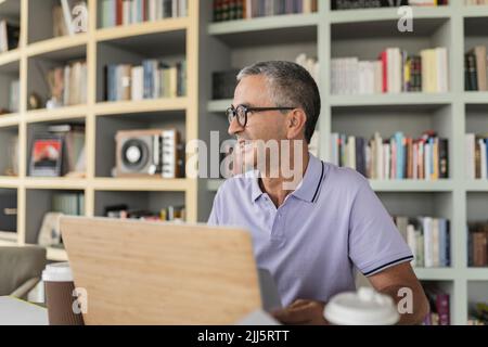 Happy mature businessman sitting in front of bookshelf Stock Photo
