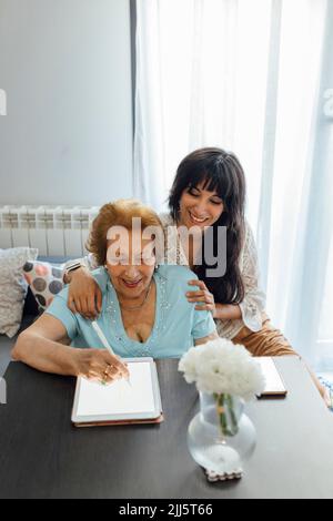 Happy woman with grandmother using tablet PC at home Stock Photo