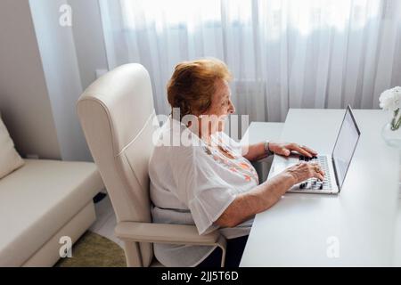 Smiling senior woman using laptop sitting at table Stock Photo