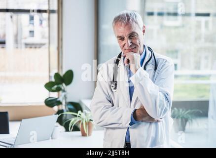 Thoughtful doctor with hand on chin standing in office Stock Photo