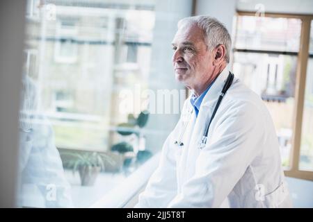 Smiling doctor looking through window at hospital Stock Photo
