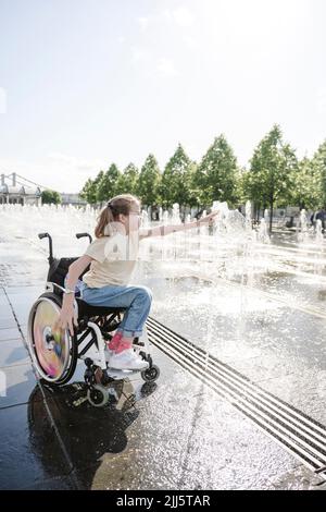 Girl sitting on wheelchair playing with fountain at park Stock Photo