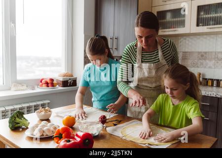 Mother assisting daughters to prepare pizza in kitchen at home Stock Photo