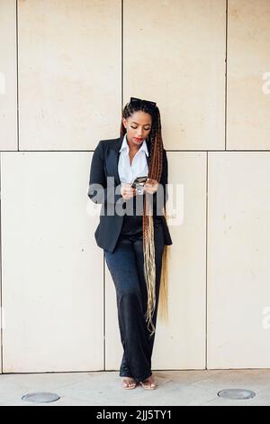 Young businesswoman using mobile phone in front of wall Stock Photo