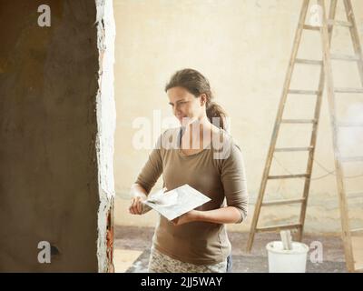 Smiling painter plastering wall with spatula in apartment Stock Photo