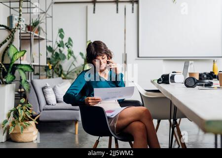 Young businesswoman with documents talking on smart phone in office Stock Photo