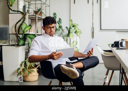 Businessman with documents using tablet PC on chair at workplace Stock Photo