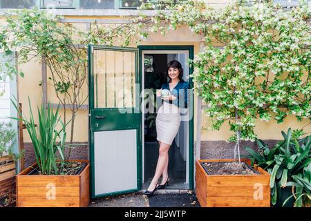 Smiling businesswoman with coffee cup at doorway Stock Photo