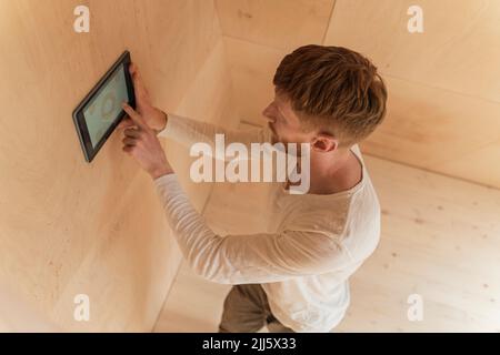 The man setting up a smart home unit with a tablet on the wall of eco home Stock Photo