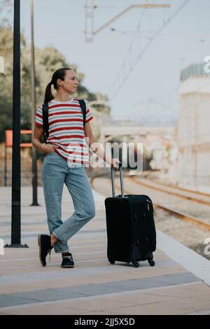 Woman with suitcase waiting for train on railway platform Stock Photo