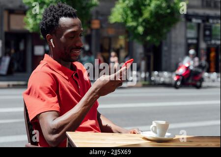 Smiling man using mobile phone sitting at cafe Stock Photo