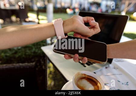 Woman paying through smart watch on mobile phone held by cashier Stock Photo
