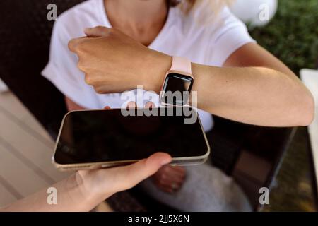 Woman making contactless payment through smart watch on mobile phone held by cashier Stock Photo