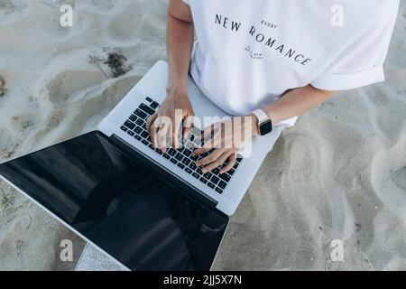 Woman using laptop sitting on sand at beach Stock Photo