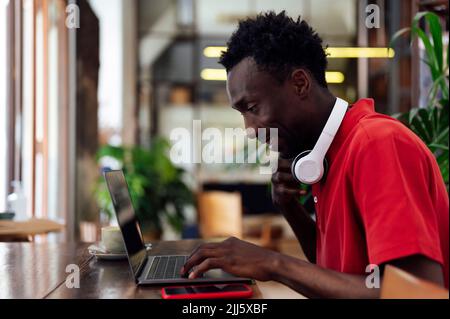 Smiling man typing on laptop sitting in cafe Stock Photo