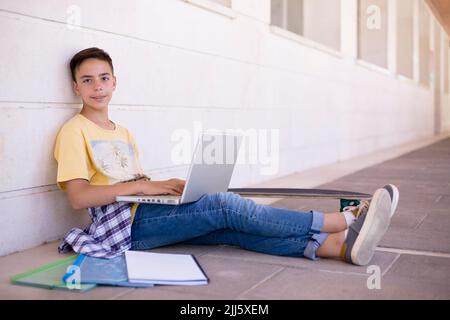 Smiling caucasian teenage boy sitting on the floor using laptop computer. Space for text. Stock Photo