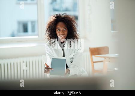Smiling female doctor with curly hair pointing at tablet PC Stock Photo