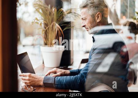 Businessman using laptop in cafe seen through glass Stock Photo