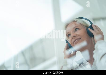 Smiling senior woman listening music seen through glass Stock Photo