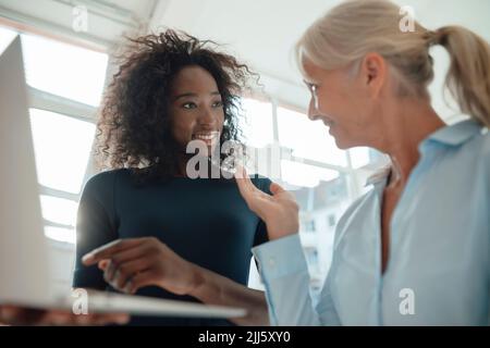 Senior businesswoman discussing with colleague holding laptop in office Stock Photo