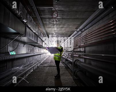 Young engineer looking at blueprint standing in tunnel Stock Photo