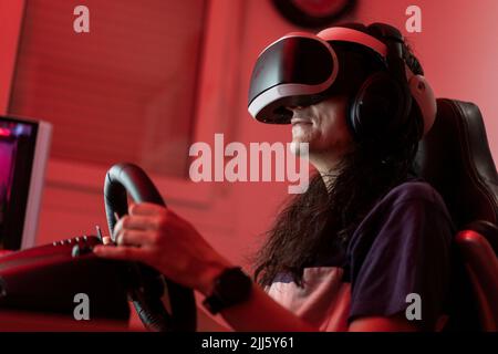 Man wearing VR glasses playing video games with steering wheel at home Stock Photo
