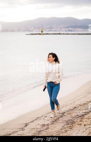 Mature woman with mobile phone walking on beach Stock Photo