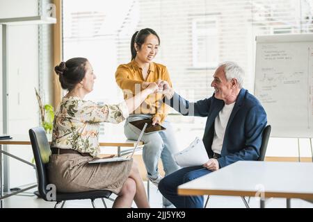 Happy multiracial business colleagues fist bumping in office Stock Photo