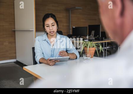 Businesswoman using tablet PC and discussing work with colleague at desk Stock Photo