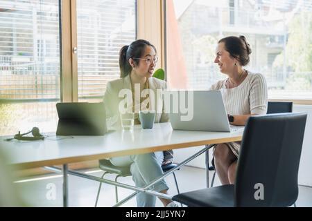 Smiling mature businesswoman with colleague discussing over laptop in office Stock Photo