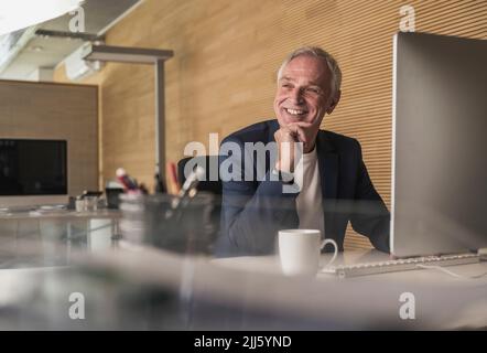 Happy senior businessman with desktop PC at work place Stock Photo