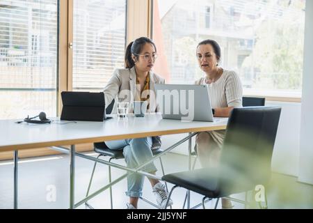 Mature businesswoman with colleague discussing over laptop in office Stock Photo