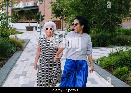 Cheerful daughter holding hands with mother walking in park Stock Photo