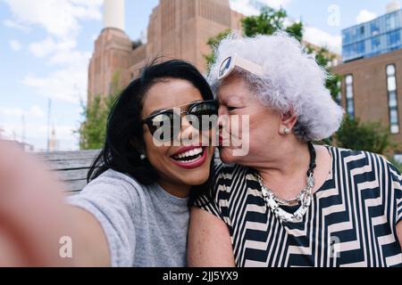 Senior woman kissing daughter taking selfie Stock Photo