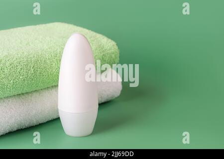 Roll on antiperspirant deodorant and bath towels on a green background. Cosmetics to reduce perspiration. Concept of personal hygiene items, body care Stock Photo