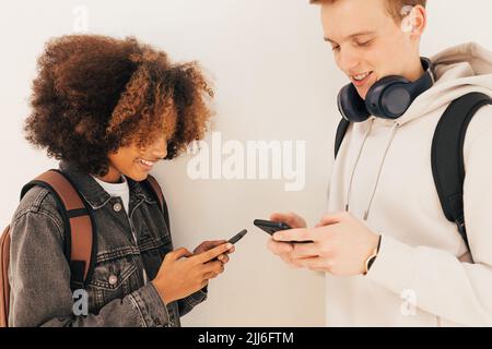 Two college students standing together at wall looking at their smartphones Stock Photo