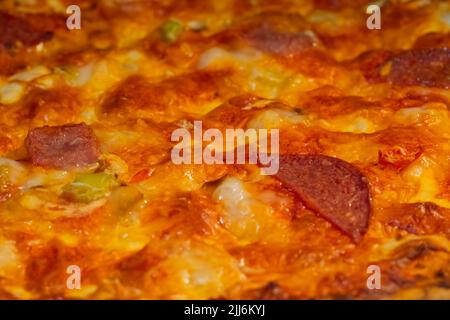 Burnt pizza with sausage, ham, pepper, cheese: close up, macro Stock Photo