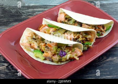 Three salmon tacos with avocado and vegetables on red serving plate Stock Photo