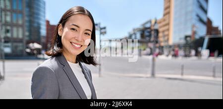 Young confident smiling Asian business woman standing on city street, banner. Stock Photo