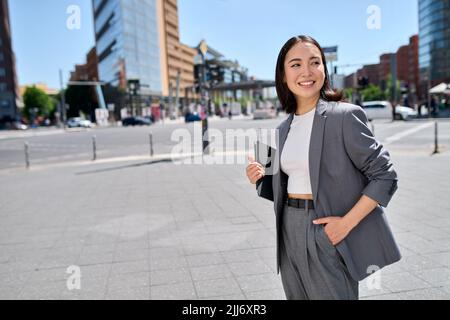 Smiling confident Asian young woman entrepreneur standing on city street. Stock Photo