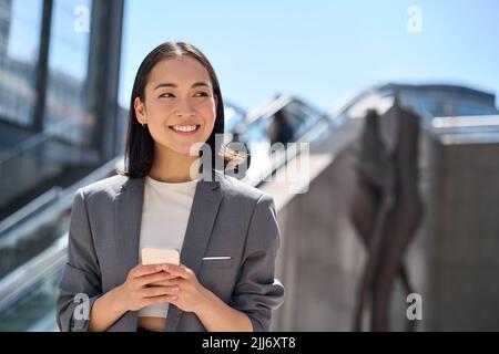 Happy young Asian business woman standing on urban city street using phone. Stock Photo