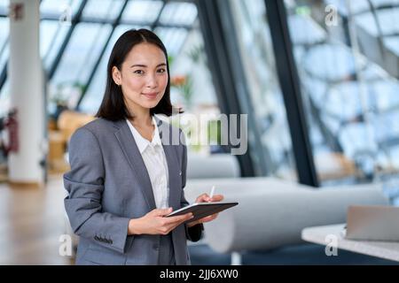 Smiling young Asian business woman leader holding digital tablet in office. Stock Photo