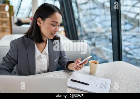 Young Asian business woman wearing suit working in office using cell phone. Stock Photo