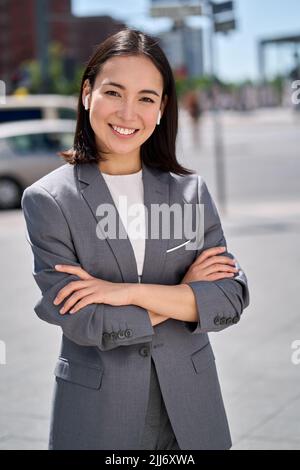 Young confident smiling Asian business woman standing on city street. Stock Photo