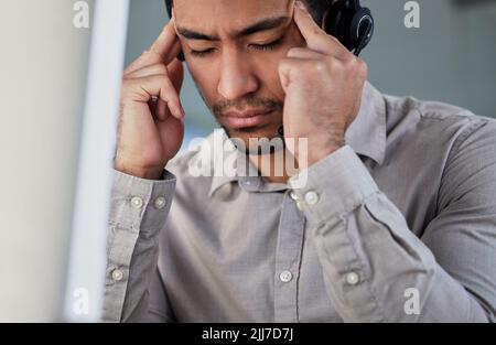 This customer is driving me crazy. a handsome young customer service agent sitting alone in the office and suffering from a headache. Stock Photo