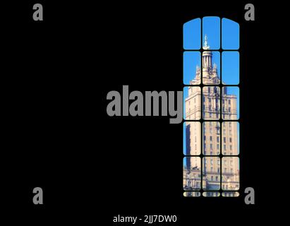 View from inside big window grid looking out at a traditional skyscraper building on blue sky copy space. Dark room with light part of a gothic Stock Photo